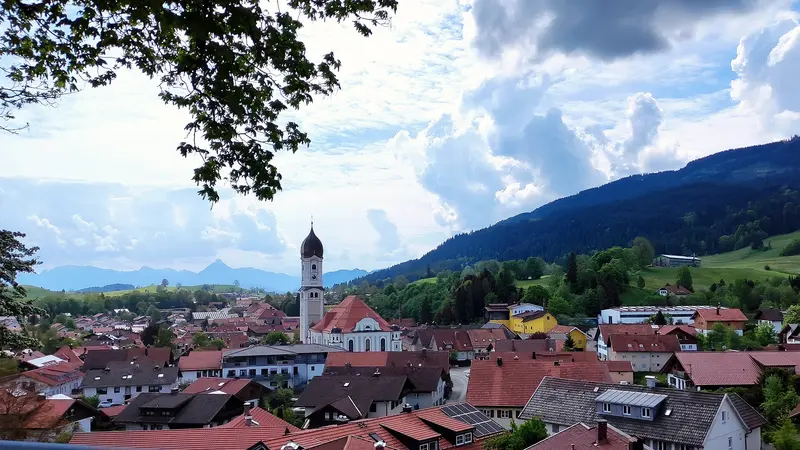 Blick über die Dächer von Nesselwang mit der Pfarrkirche St. Andreas und bewaldeten Bergen im Hintergrund