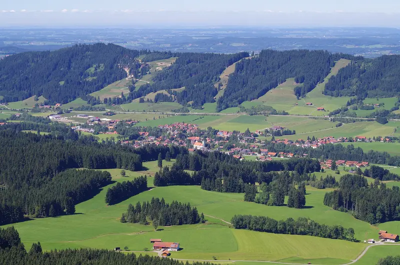 Blick von oben auf das Weitnauer Tal mit dem Ort Weitnau, Wiesen und bewaldeten Hügeln