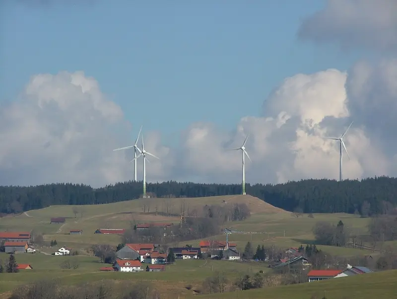Windkraftanlagen auf einem bewaldeten Höhenzug über Wildpoldsried, im Vordergrund Höfe und Wiesen