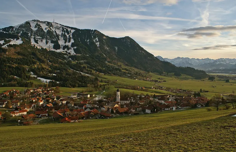 Rettenberg von Norden mit Pfarrkirche St. Stephan, dahinter der Grünten und die Allgäuer Alpen