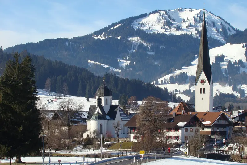 Fischen im Allgäu im Winter mit Frauenkapelle und dem spitzen Turm der Pfarrkirche St. Verena vor verschneiten Bergen
