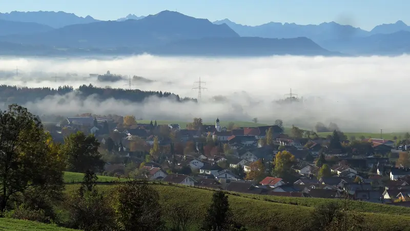Börwang von Norden mit Kirchturm, darüber Nebelbänke und die Gipfel der Allgäuer Alpen