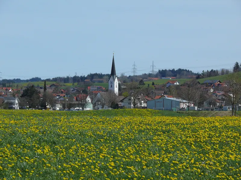 Blick über eine Löwenzahnwiese auf den Ortskern von Durach mit Pfarrkirche