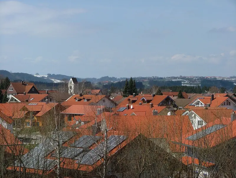 Blick vom Kirchenbühl über die roten Ziegeldächer von Lauben im Oberallgäu mit Kirchturm und Hügeln im Hintergrund